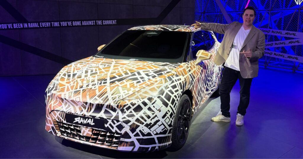 Christoffer står bredvid en maskerad elbil i ett blått rum.